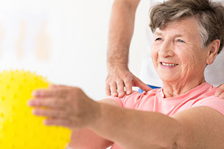 Elderly woman smiling while doing arm exercises with a yellow ball