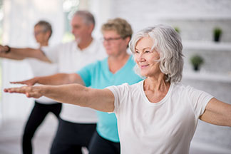 Senior women and men in an exercise class at a community center doing arm stretches.