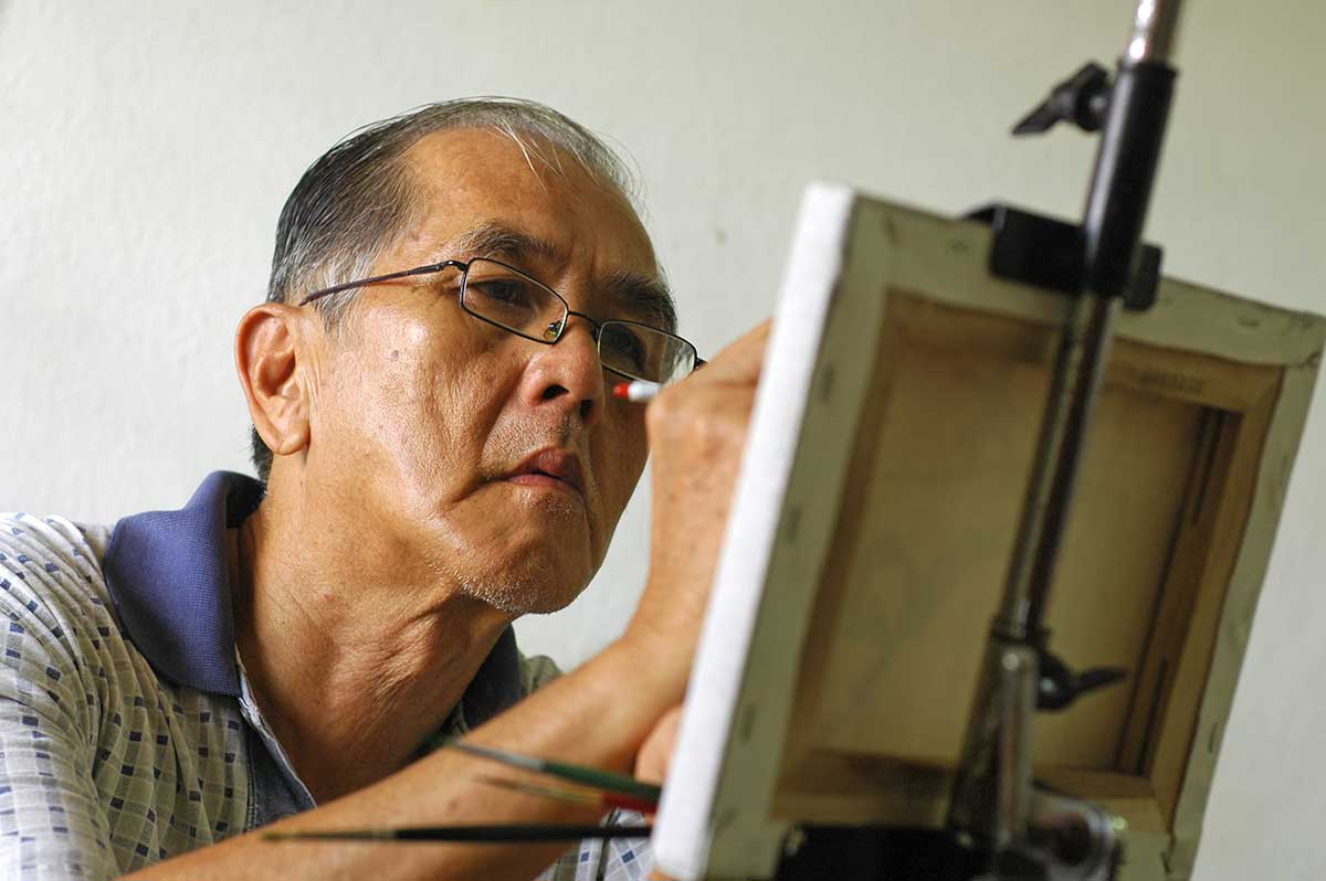 Senior man concentrating on painting a canvas in a well-lit room.