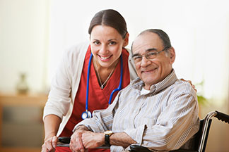 Smiling caregiver in a red uniform and senior man sitting in a wheelchair in a bright room.