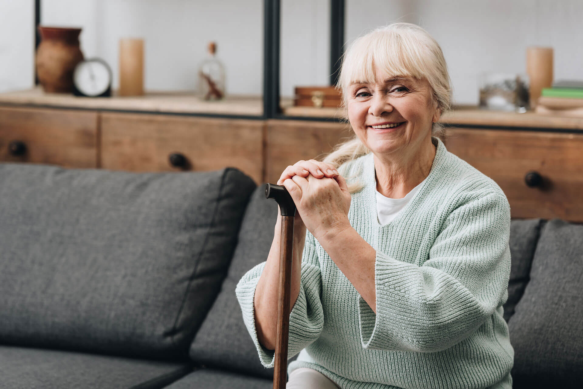 Elderly woman smiling while sitting on a sofa with her hands on a walking cane