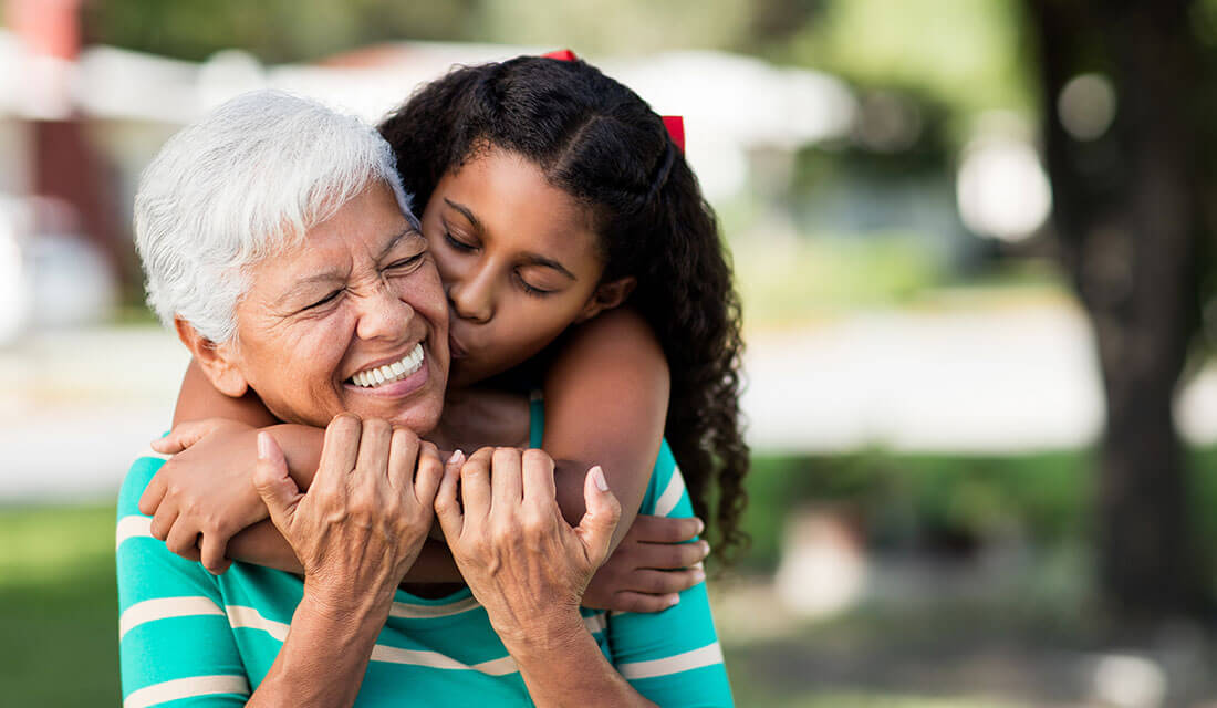 Elderly woman with gray hair joyfully embraced by a young girl in a park.