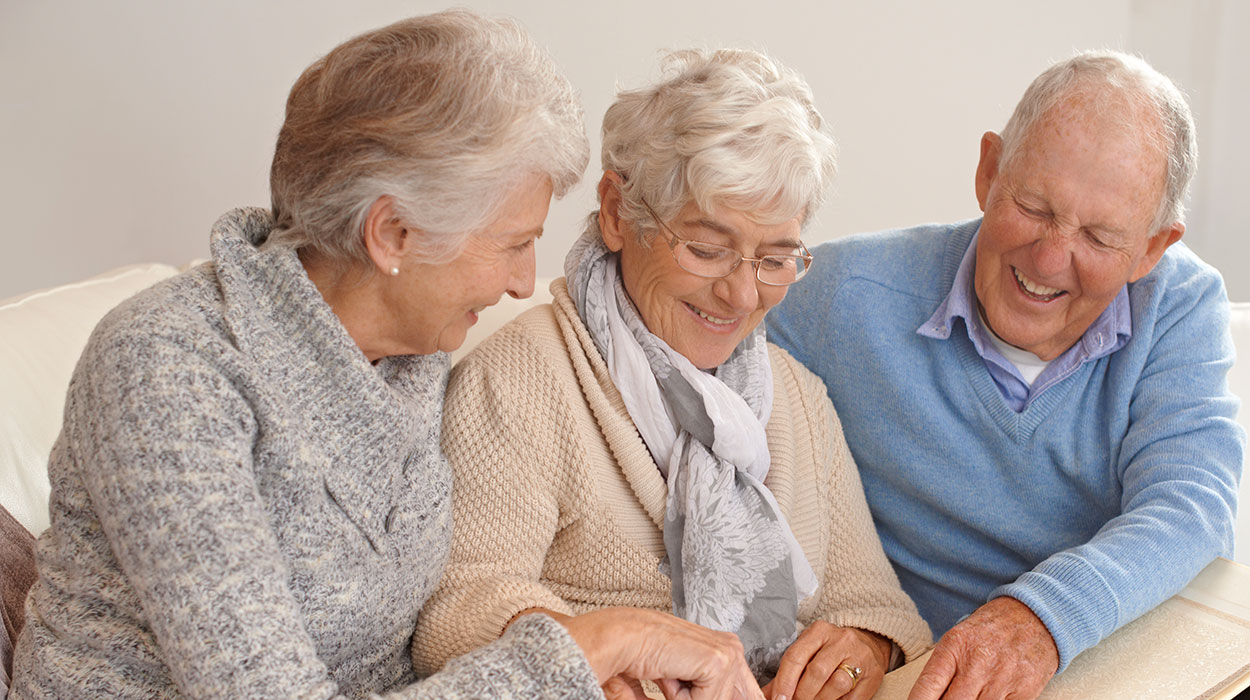 Three seniors smile while engaging in a group activity on a table.