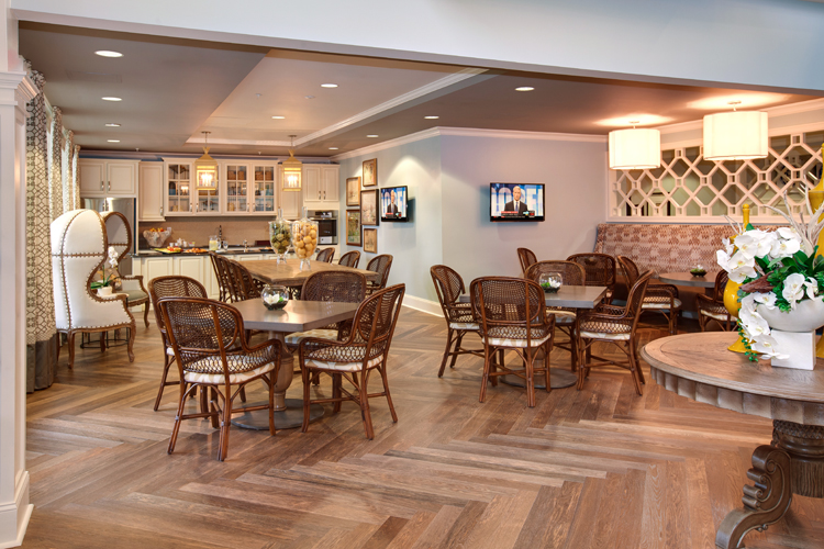 Cozy cafe area with wicker chairs, tables, and a kitchen in a senior living community.