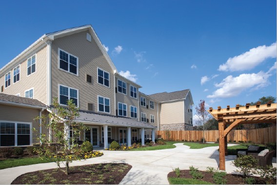 Exterior view of a senior living community building with a landscaped courtyard and seating area.