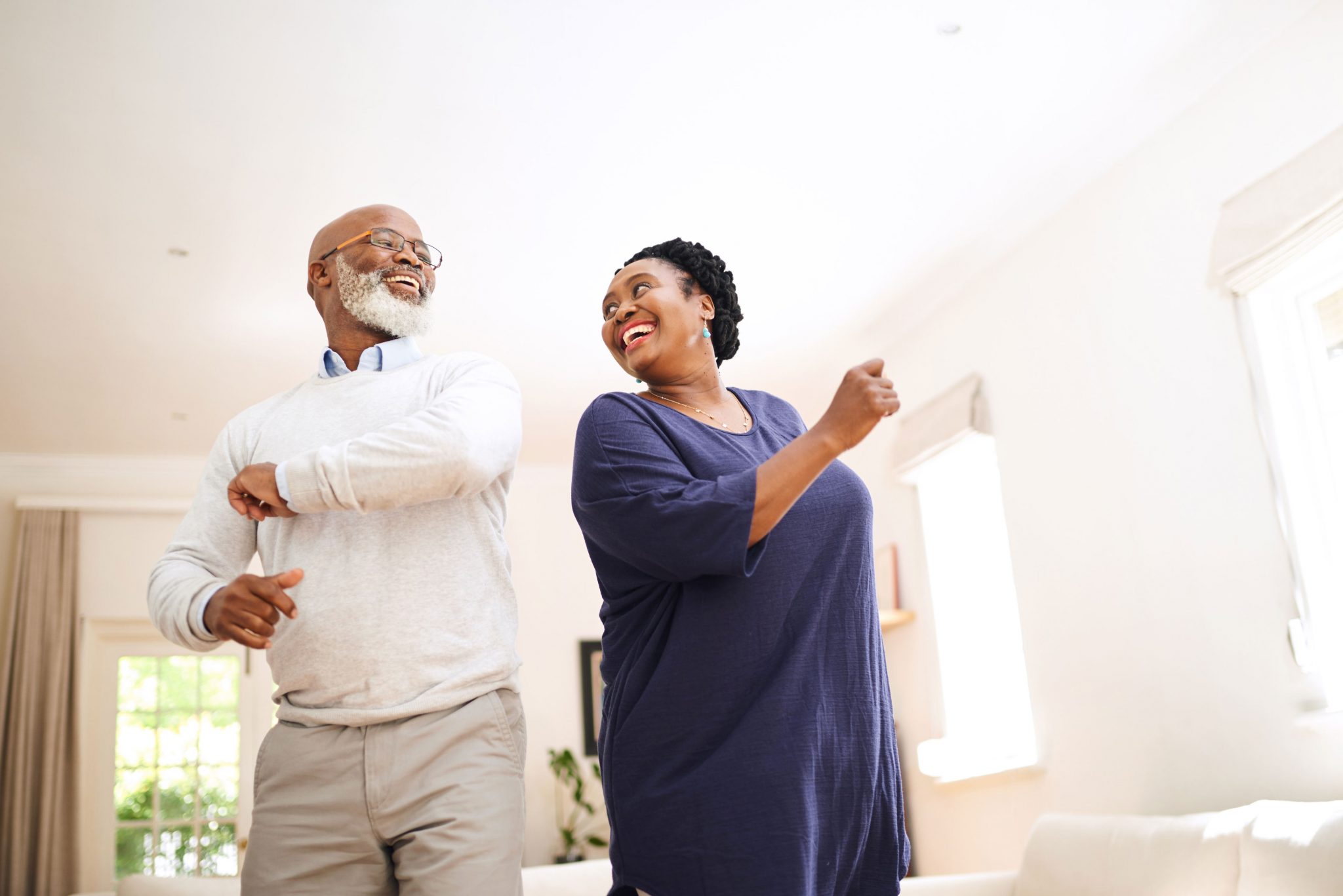Two seniors dancing together in a bright living room, smiling with joy.