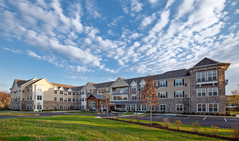 Exterior view of a large senior living community building with manicured lawns under a blue sky.