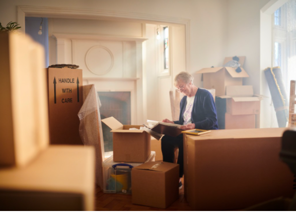 Senior woman packing and sorting through boxes in a brightly lit room.