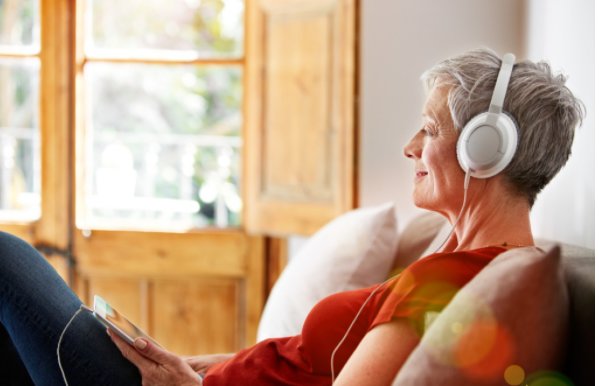 Senior woman with headphones enjoying music on a sofa in a bright living room.