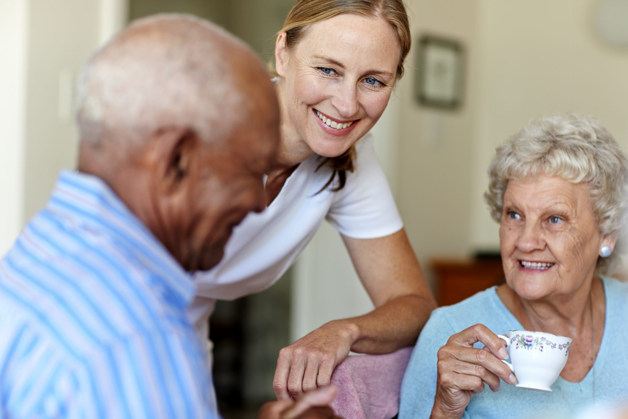 Caregiver smiling and interacting with two senior residents in a living unit.
